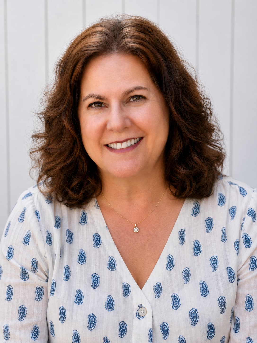 Smiling woman with shoulder-length brown hair wearing a light blue paisley-patterned blouse.