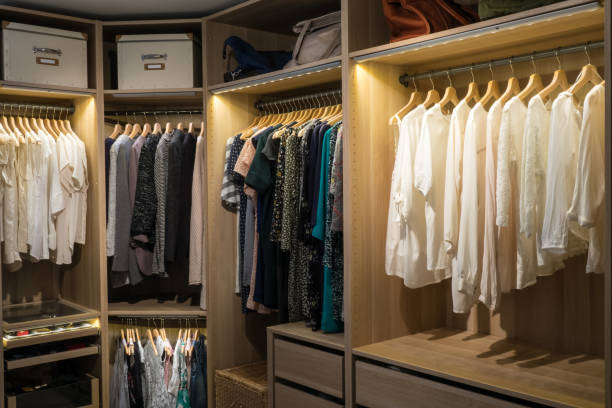 Luxury walk in closet / dressing room with lighting and jewel display. Dresses, handbags, blouses and sweaters on hangers in the wardrobes. Hoizontal.
