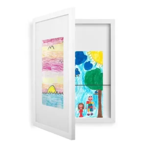 A white picture frame displays children's artwork. One side shows a colorful sunset over the ocean with birds above. The other side features a bright scene with a tree, a rainbow, and two people, one in a dress and one with multicolored clothes.