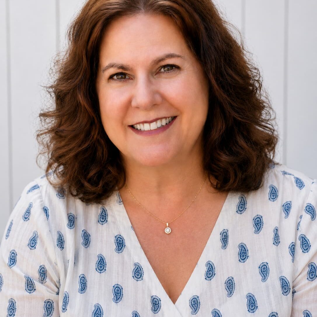 Smiling woman with shoulder-length brown hair wearing a light blue paisley-patterned blouse.