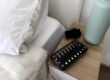 Bedside scene with a wooden nightstand, a teal lamp, and a smartphone showing alarm times on screen as alarms glow.